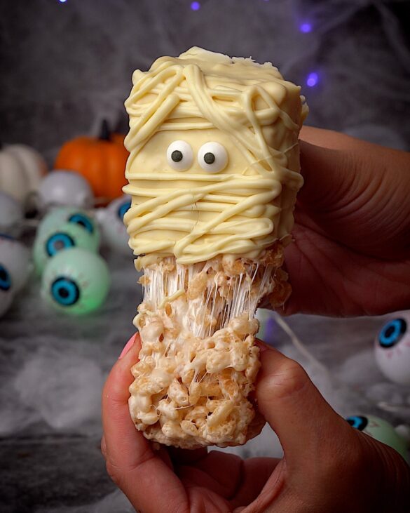 “Gooey mummy Rice Krispie treat being pulled apart to show melted marshmallow inside – easy no-bake Halloween dessert.