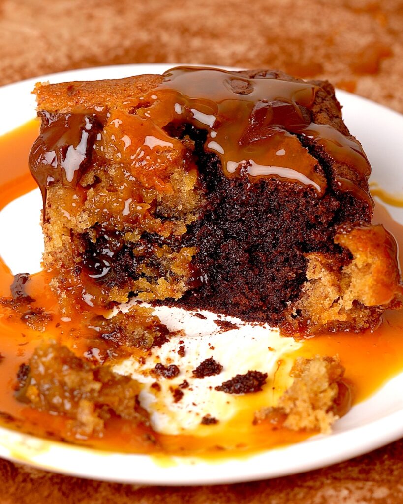 Sticky toffee pudding brownie on a plate with caramel sauce drizzled on top and a piece missing to show the inside.