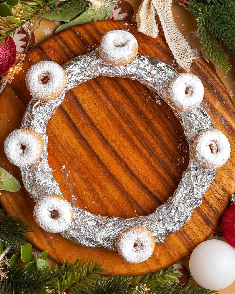 Easy-Christmas-Doughnut-wreath-three-Ingredient.jpg - Ems Foodie Fix Adding mini doughnuts onto a foil ring to make a Christmas wreath.