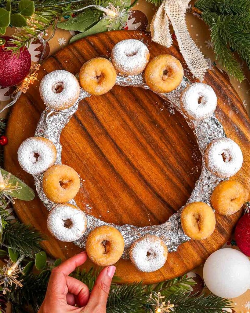 Easy-Christmas-Doughnut-wreath-three-Ingredient.jpg - Ems Foodie Fix Adding mini doughnuts onto a foil ring to make a Christmas wreath.