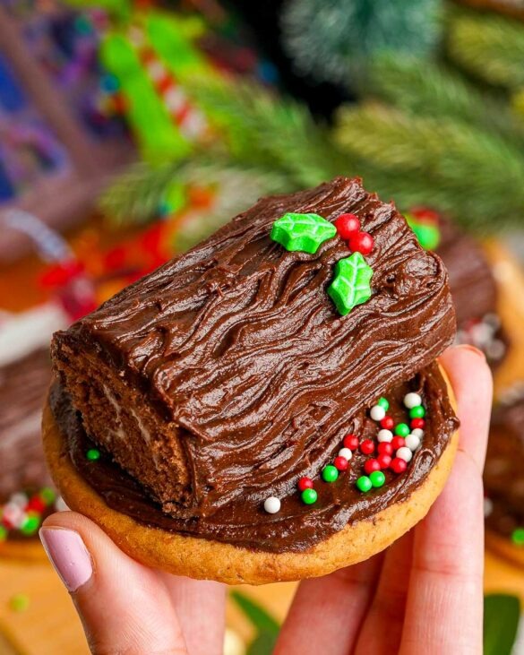 Yule log cookie held in the air with a holly sugar decoration on top.