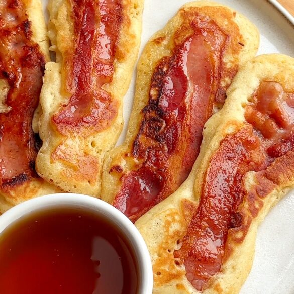 Bacon pancake dippers on a plate with a pot of maple syrup.