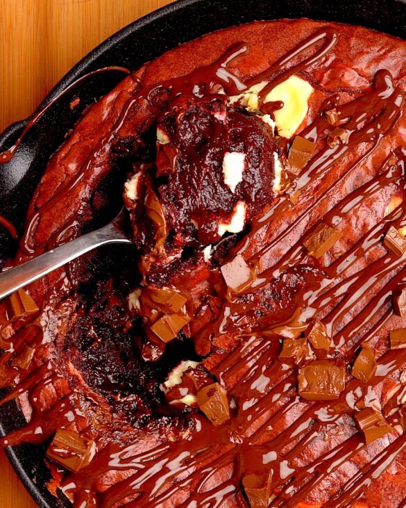 Red velvet cheesecake brownie skillet with a scoop on a spoon.