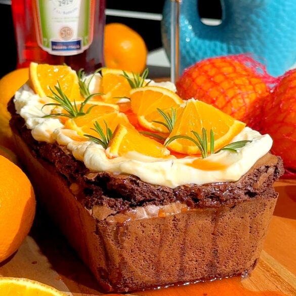 Aperol spritz cheesecake loaf with orange slices and rosemary on top.