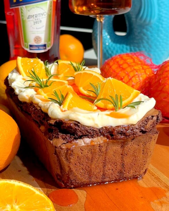 Aperol spritz cheesecake loaf with orange slices and rosemary on top.