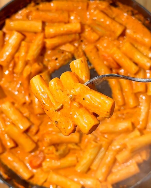 Fork lifting orange-coated pestp vodka rigatoni pasta on a fork.