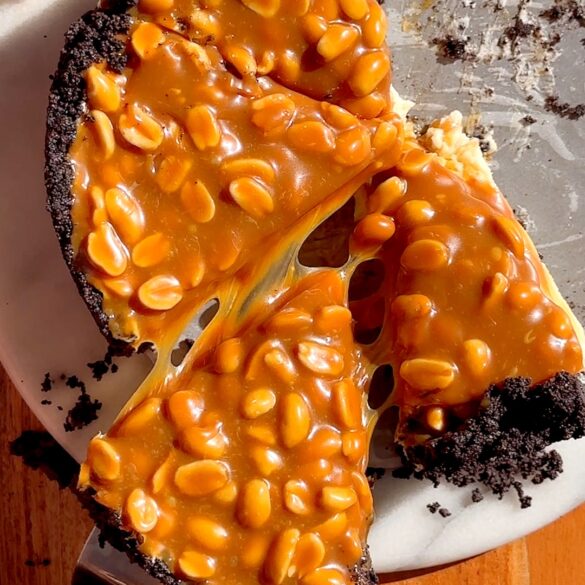 Snickers cheesecake thats been sliced with one slice being pulled out with a cake slice.