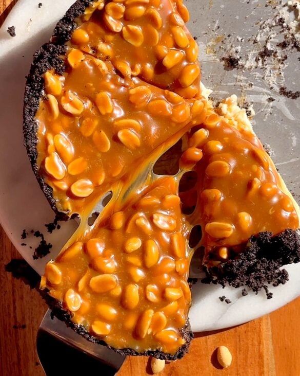 Snickers cheesecake thats been sliced with one slice being pulled out with a cake slice.